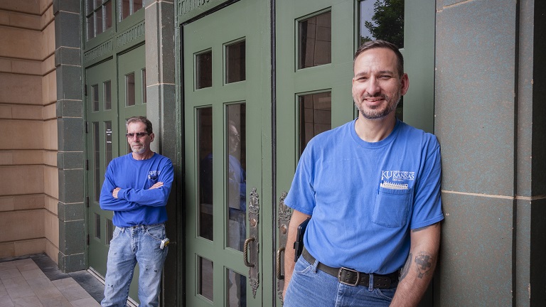 KU carpenter Jeremy Mills and painter Clint Johnston standing in front of Strong Hall doors